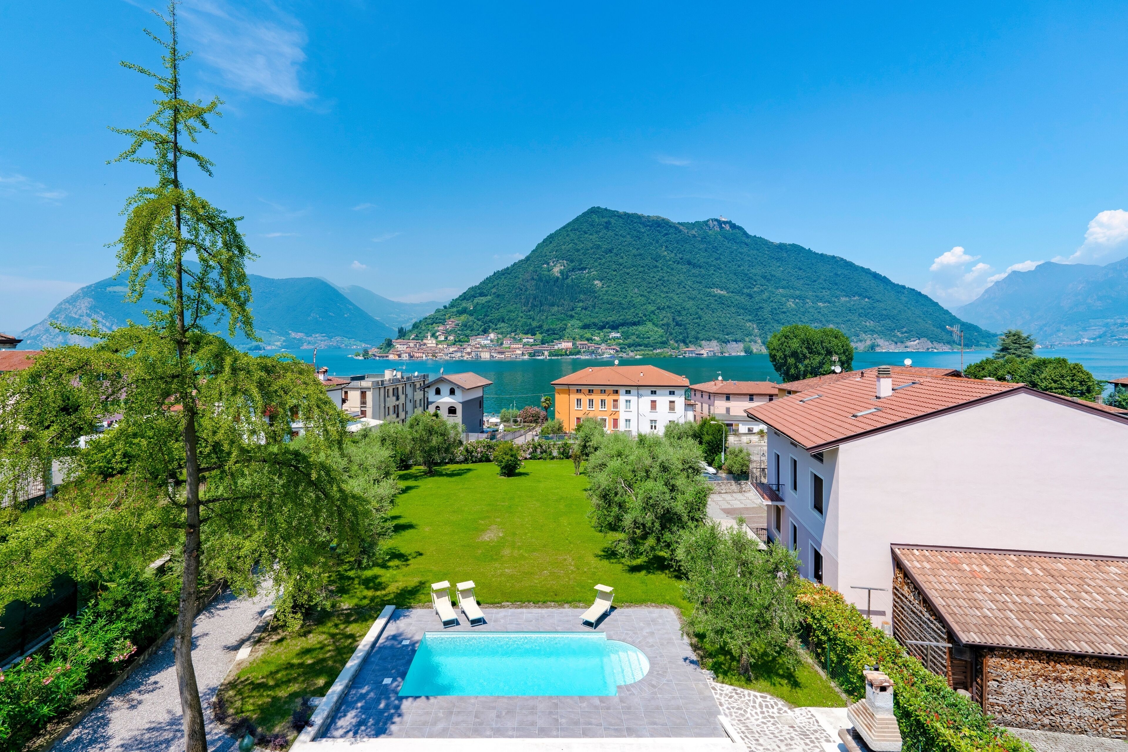 Ein Poolbereich mit Liegestühlen, freier Seeblick und Gebäude im Hintergrund.