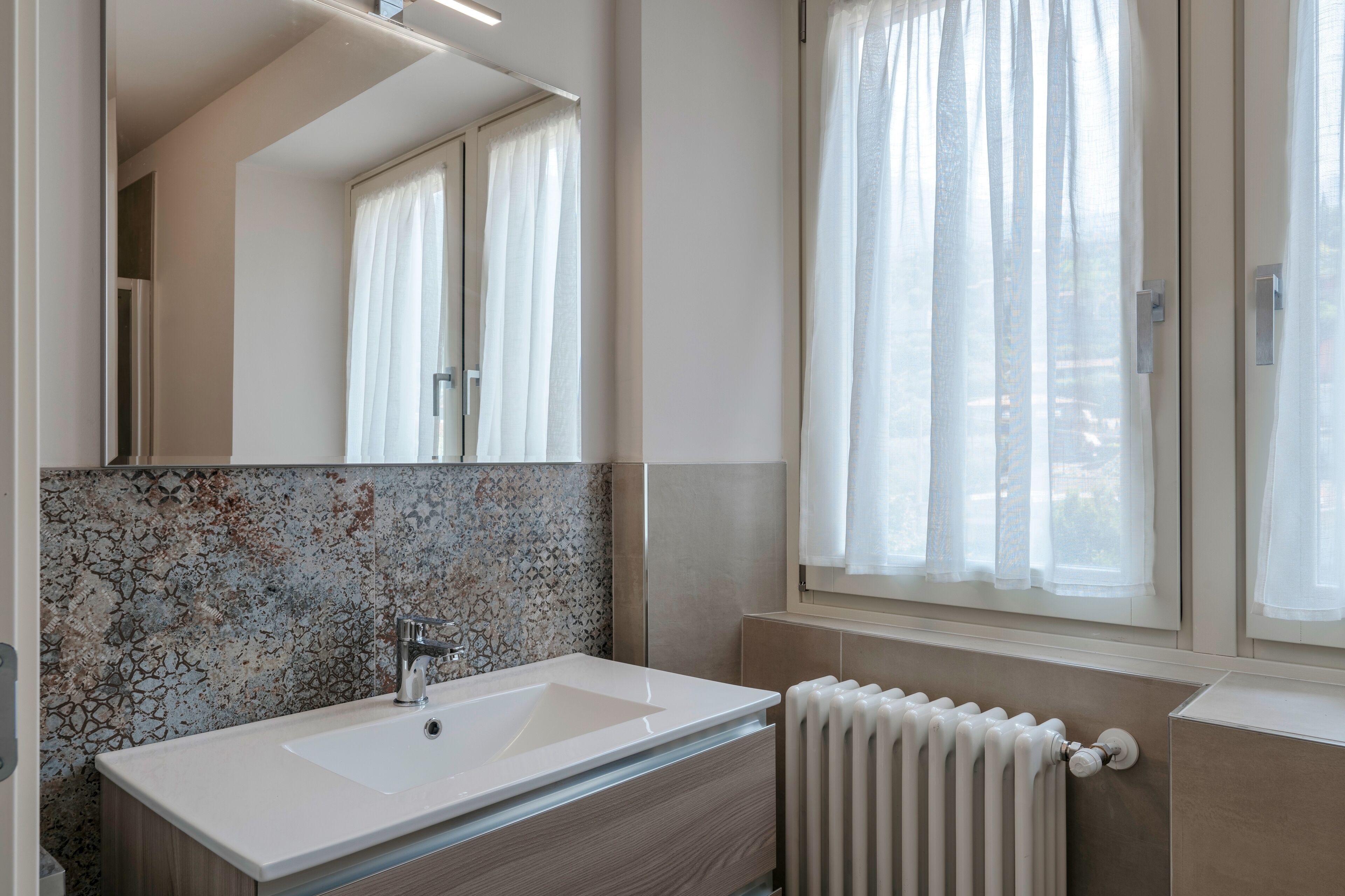 A modern bathroom with a large mirror, a white sink, and a tiled backsplash.