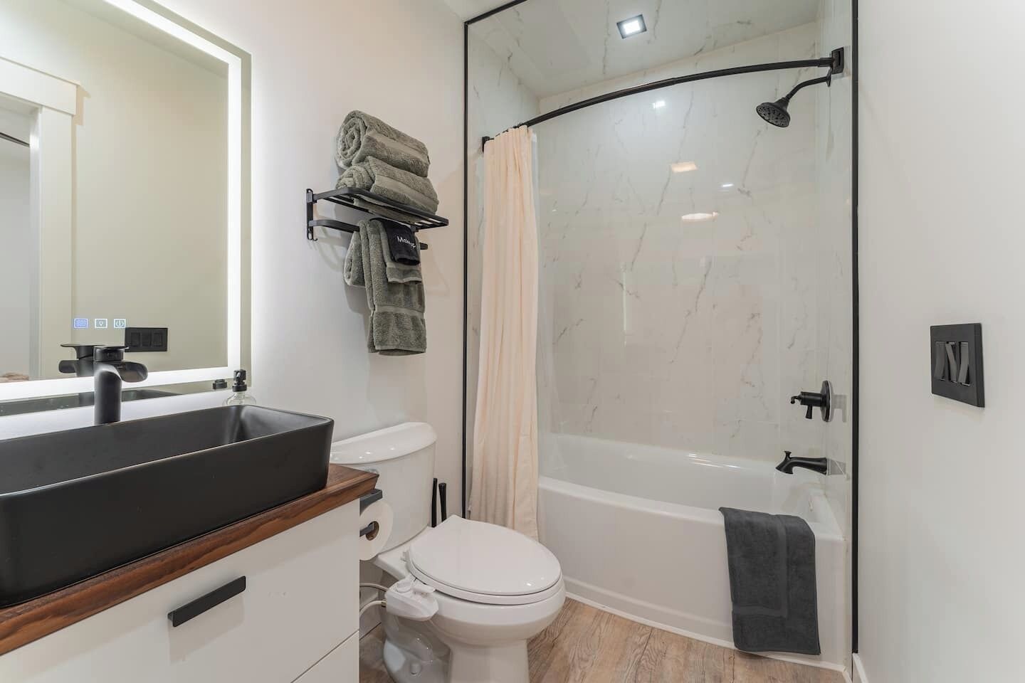 A modern bathroom with a black sink, white toilet, and a glass-enclosed shower.
