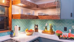 Une cuisine moderne avec un dosseret de couleur turquoise, des meubles hauts en bois et une variété de fruits et d’ustensiles de cuisine disposés sur le plan de travail.