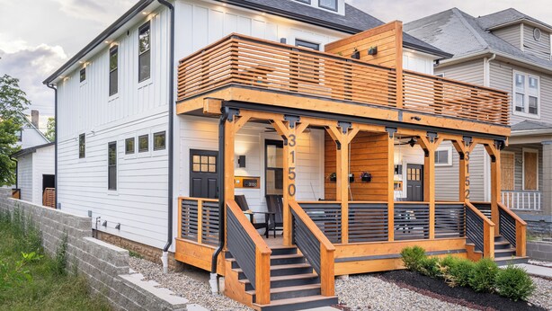 Une maison à deux étages avec une terrasse en bois et un escalier menant à un porche abrité.