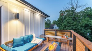 A deck with a wooden bench, a blue sofa with cushions, and a fire feature. - Artisan Oasis-Hot Tub | Fire Pit 4BD Right Unit (Indianapolis)