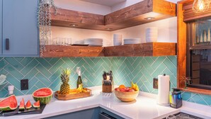 A kitchen with wooden shelves, a tiled backsplash, and various kitchen items like a cutting board, fruit, and a coffee maker. - Artisan Oasis-Hot Tub | Fire Pit 4BD Right Unit (Indianapolis)