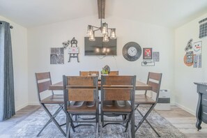 Un espace repas comprenant une table et des chaises en bois, un lustre, des œuvres d’art murales et une horloge.