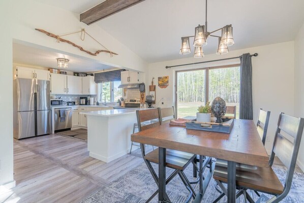 A modern kitchen with stainless steel appliances, a central island, and a dining area with a wooden table and metal chairs.