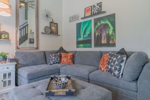 A modern living room with a grey sectional sofa, decorative pillows, a coffee table with a bowl, a mirror, and framed artwork on the wall. - The Vasi Landing Pad (Fairbanks North Star Borough)