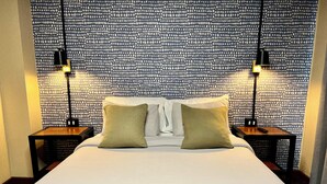 Una cama bien hecha con dos almohadas, una mesita de noche con una lámpara y un papel tapiz estampado.