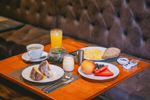A breakfast tray with bread, fruit, eggs, and a glass of orange juice on a wooden table. - Tinka     (Santiago)