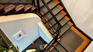 Una escalera con barandilla de metal, peldaños de madera y un rellano alfombrado.