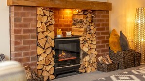 A fireplace with a brick surround, a modern TV mounted above it, and decorative items on the mantel. - Charming Modern Retreat with Private Garden - Pass the Keys (Market Drayton)