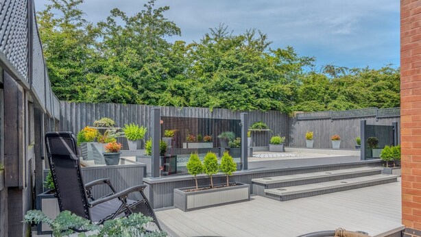 A modern outdoor patio with a glass table, wicker chair, and a grill area. - Charming Modern Retreat with Private Garden - Pass the Keys (Market Drayton)