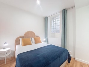 A bedroom with a bed, a bedside table, a window with curtains, and a view of the outside.