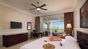 A hotel room with a bed, a desk, a chair, a TV, and a balcony with curtains. - Presidential Junior Suite - Cabarete (Puerto Plata)