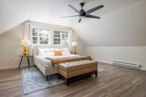 A bedroom with a bed, a ceiling fan, a window, and a radiator.