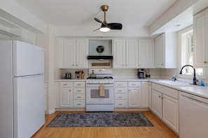 A kitchen with white cabinets, a stove, a refrigerator, and a ceiling fan.