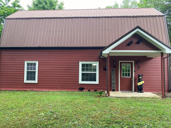 Cozy cabin with a gabled roof and a small porch, featuring two windows and a door with a welcoming entrance.