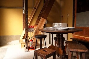 A round table with stools, a fire extinguisher, and wooden beams in a room with a yellow wall. - Higashi Matsuyacho East (Kyoto)