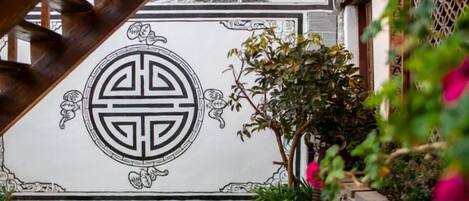 Un mur d’architecture chinoise traditionnelle orné d’un motif géométrique, une pelouse artificielle verte et des plantes en pot.
