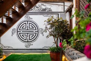 A traditional Chinese architectural wall with a geometric pattern, a green artificial lawn, and potted plants.