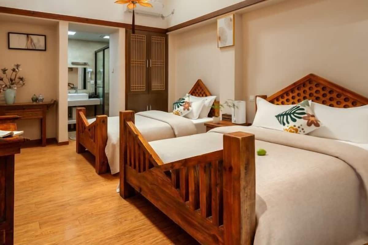 A hotel room with two wooden beds, a wooden desk, a mirror, and a small table with a vase.