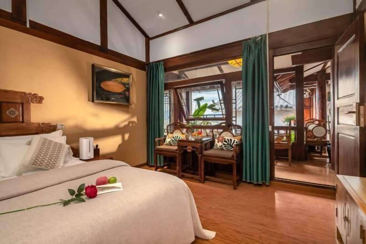 A hotel room with a bed, a desk, chairs, a window with curtains, and a view of the outside.