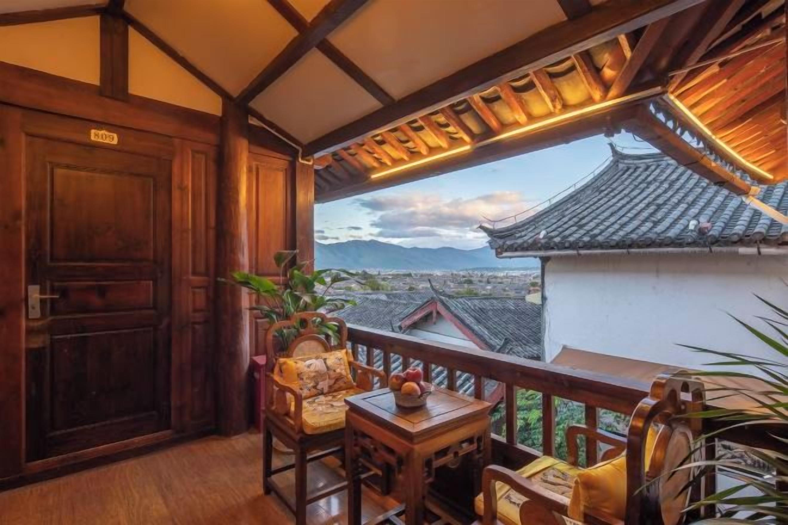 A balcony with traditional wooden furniture, a view of a cityscape, and a traditional building in the background.