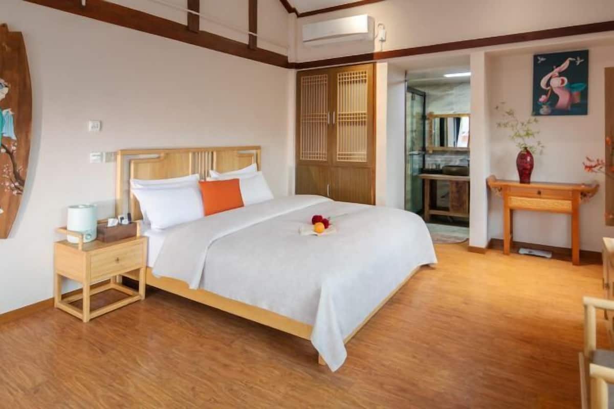 A bedroom with a wooden bed, a nightstand, a small table, and a wall-mounted air conditioner.