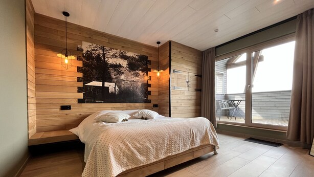 A modern bedroom with a wooden headboard, a large window with curtains, and a view of the outdoors. - Lu T'Chêne - dans le Village d'Opont (Opont)