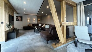 A modern living room with a large wooden beam structure, a sectional sofa, a dining area, and a large window with curtains. - Lu T'Chêne - dans le Village d'Opont (Opont)