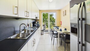 Una cocina moderna con electrodomésticos de acero inoxidable, un comedor con mesa y sillas, y un ventanal corredero que da a un balcón.