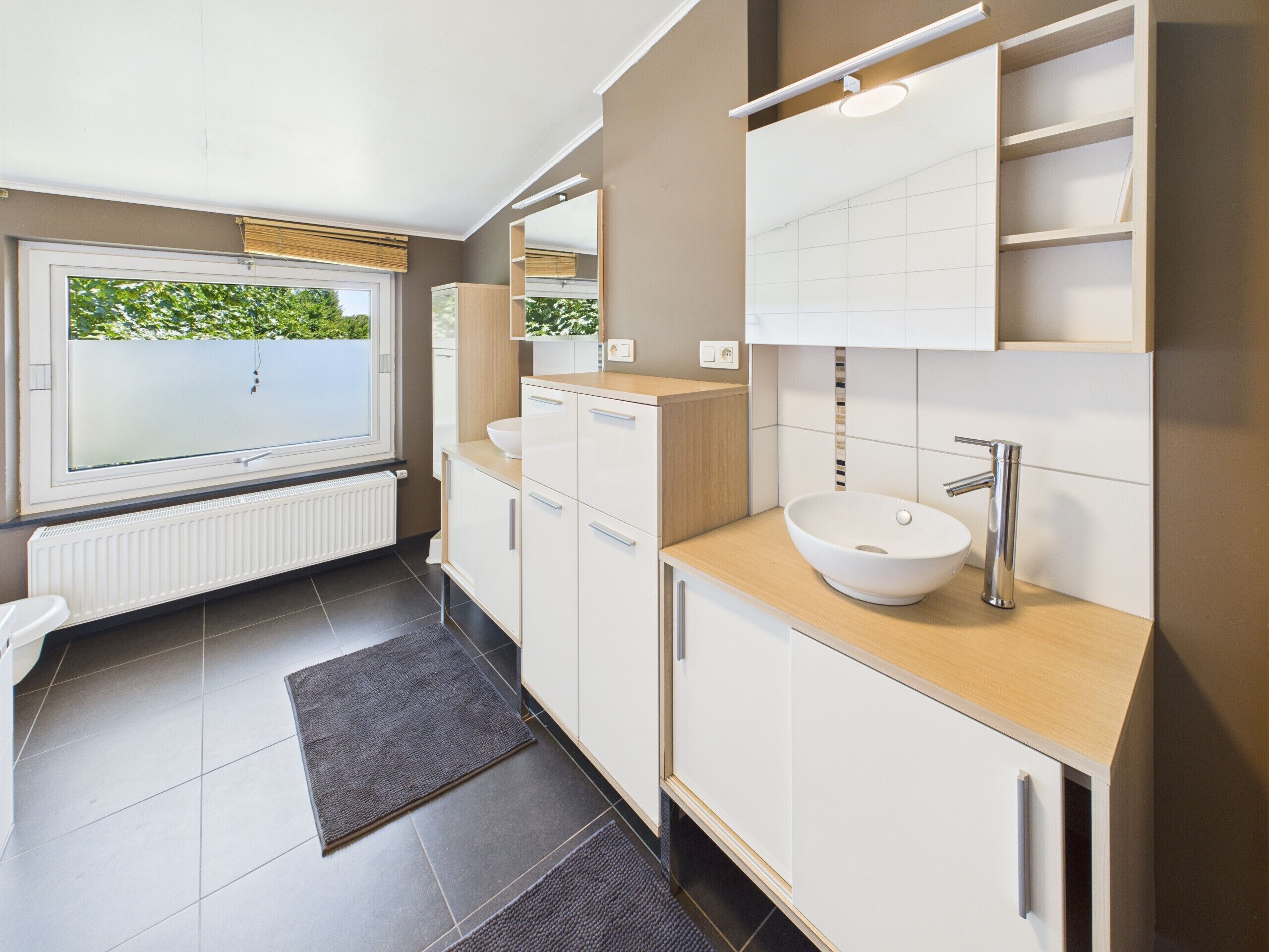 Een moderne badkamer met een groot raam, een inbouwspoelbak en een spiegel boven het aanrecht.