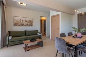 Un salon moderne avec un canapé vert, une table basse en bois et une table à manger avec des chaises. Un tableau est accroché au mur et une plante est posée sur la table à manger.