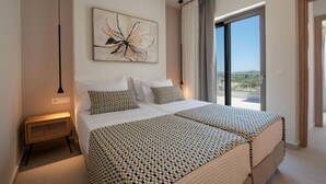 Habitación de hotel moderna con una cama grande, una mesita de noche, una obra de arte en la pared y vistas a través de un ventanal amplio.