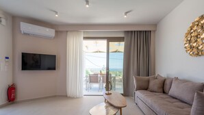Una sala de estar moderna con un televisor de pantalla plana, un sofá, una mesita y vistas al exterior a través de una puerta corrediza de vidrio.