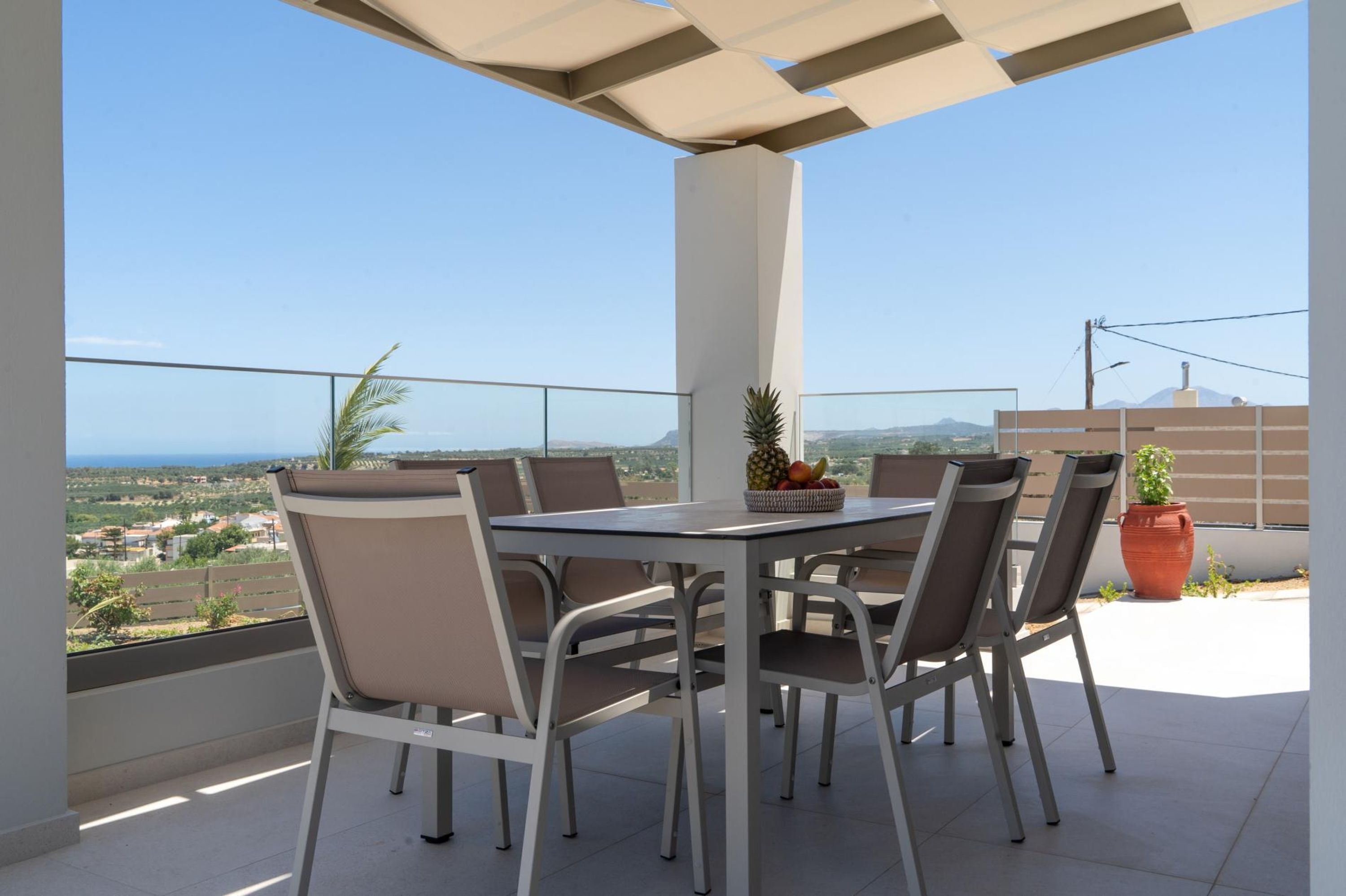 A balcony with a table and chairs, a potted plant, and a view of the landscape.