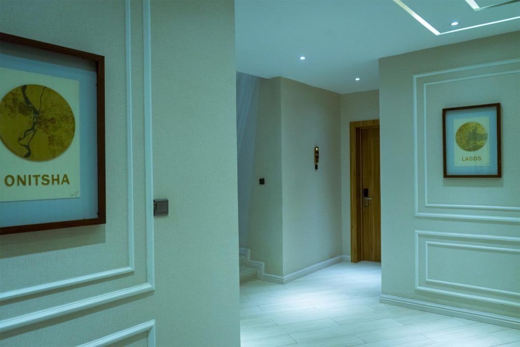 A hallway with framed artwork on the walls, a wooden door at the end, and a light-colored floor.