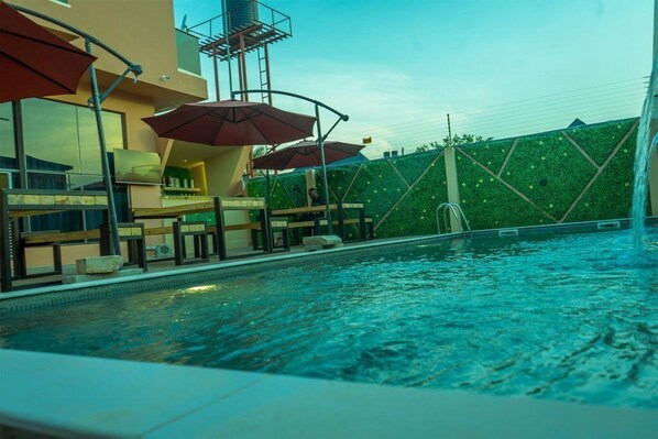 A swimming pool with a green wall and umbrellas. - 649 Suites (Asaba)