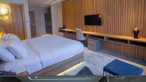A hotel room with a bed, a desk, a TV, and a wardrobe. - 649 Suites (Asaba)