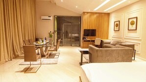 A modern hotel room with a large bed, a dining area with a table and chairs, a sofa, a TV, and a sliding glass door leading to a balcony. - 649 Suites (Asaba)