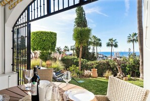 An outdoor dining area with a view of the sea, featuring a table set with wine glasses and a bottle, surrounded by wicker furniture. - Pool and Garden Apt by Costarentals - Ref 253 (Las Lagunas de Mijas)