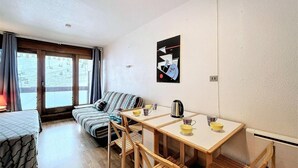 Une pièce de taille modeste, comprenant un canapé, une petite table à manger et une fenêtre avec des rideaux.