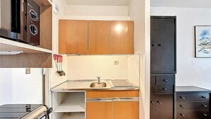 Une cuisine de taille réduite, dotée de meubles de rangement en bois, d’un évier, d’une cuisinière et d’un réfrigérateur.