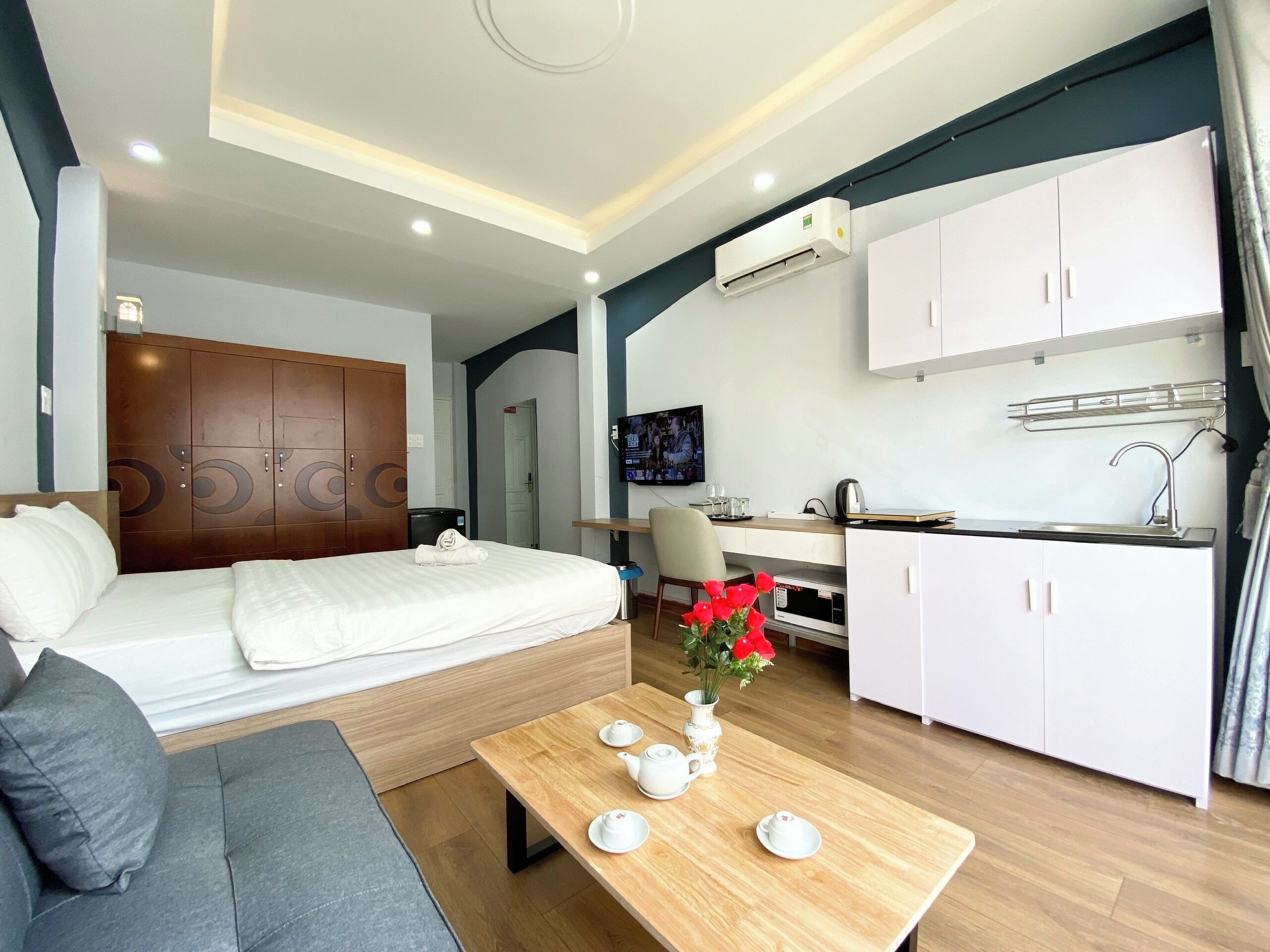 Una moderna camera d'hotel con un letto, una poltrona, un tavolo da pranzo con servizi da tè, un angolo cottura e una TV.