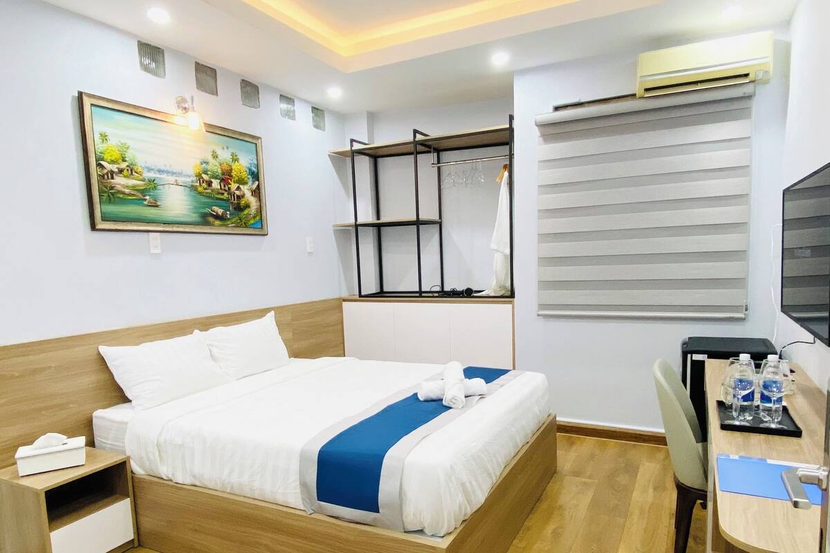 Ein Hotelzimmer mit Bett, Schreibtisch, Stuhl, Klimaanlage und einem Bild an der Wand.