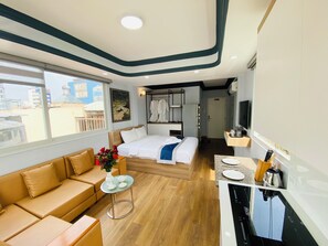 A modern hotel room with a bed, sofa, small table, and kitchenette.