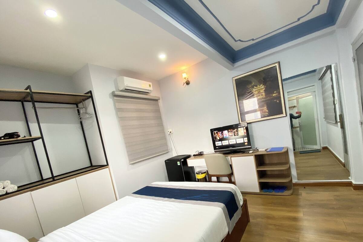 Ein Hotelzimmer mit einem Bett, einem Schreibtisch mit Computer, einem Fernseher und einem Fenster mit Jalousien.