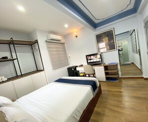 A hotel room with a bed, a desk with a computer, a TV, and a window with blinds.