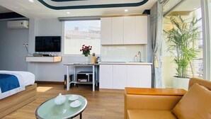 Una camera d'albergo moderna con un letto, un piccolo tavolo con teiere, una poltrona, angolo cottura, televisione e un'ampia finestra con una pianta.