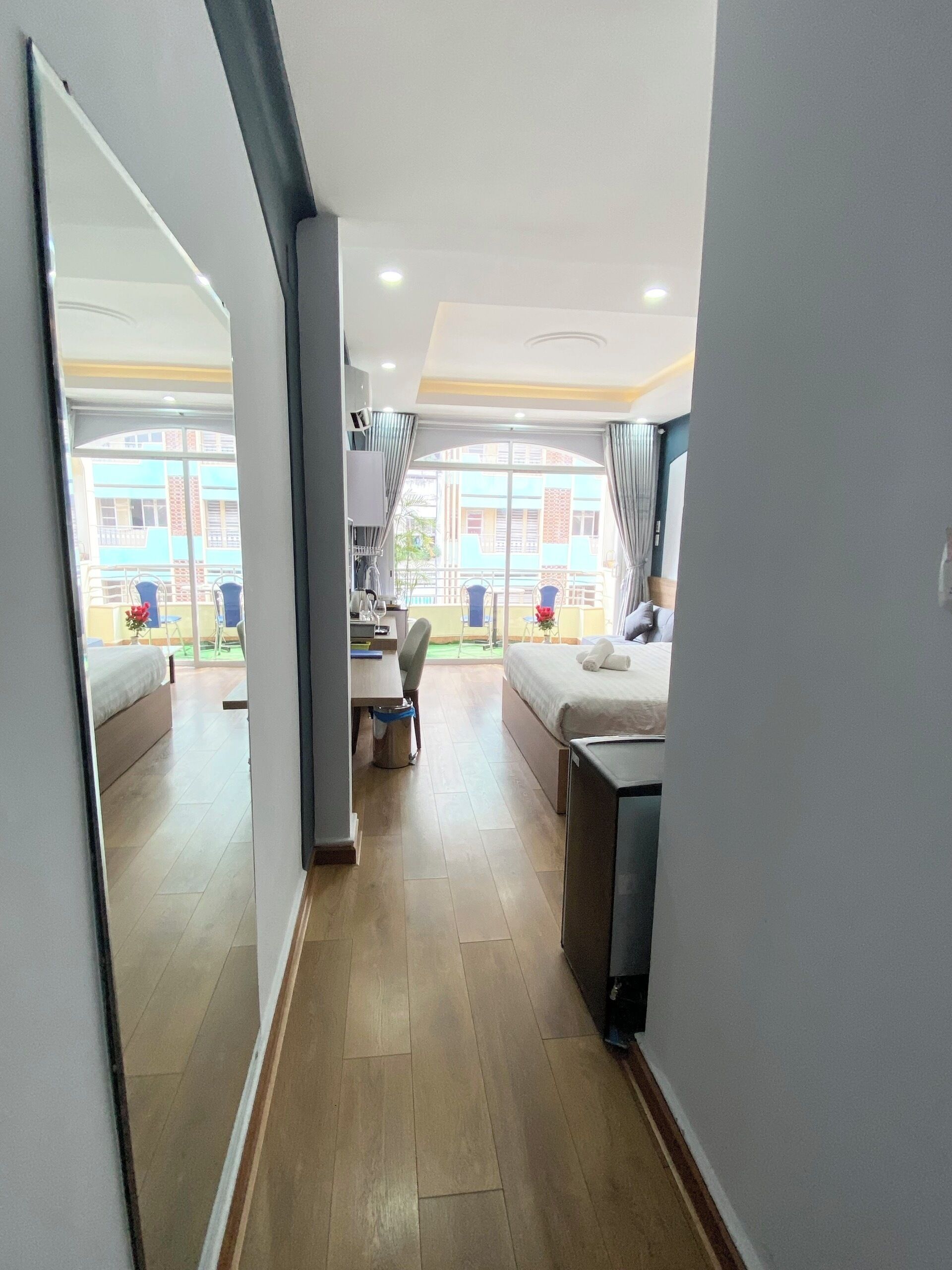 Habitación de hotel con cama, escritorio, silla, una mesita, espejo y vistas al balcón exterior.