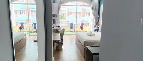 Habitación de hotel con cama, escritorio, silla, una mesita, espejo y vistas al balcón exterior.